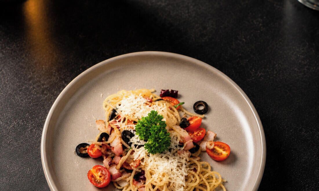 A plate of spaghetti with tomatoes, olives, and cheese.