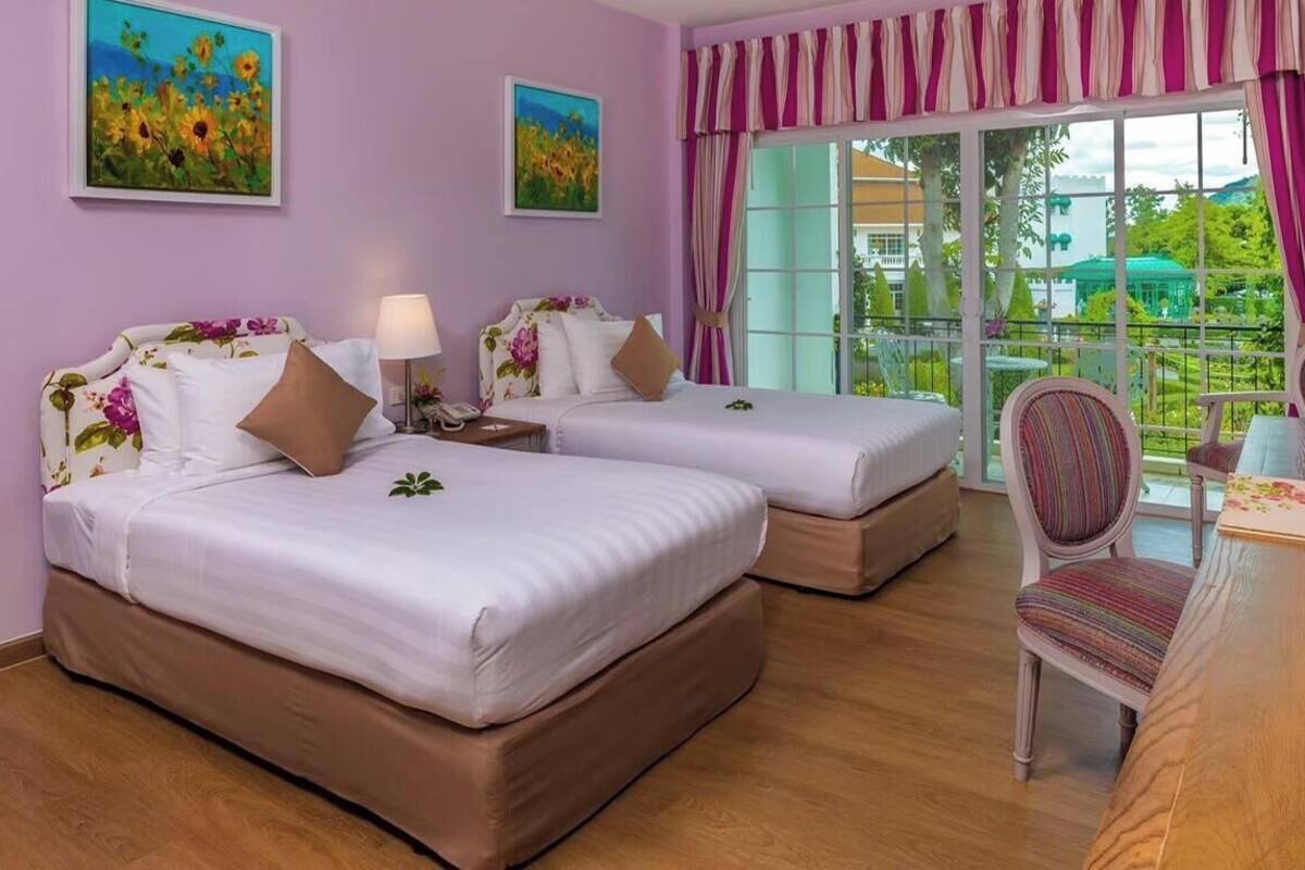 A hotel room with two beds, a desk, a chair, and a view of the outdoors.