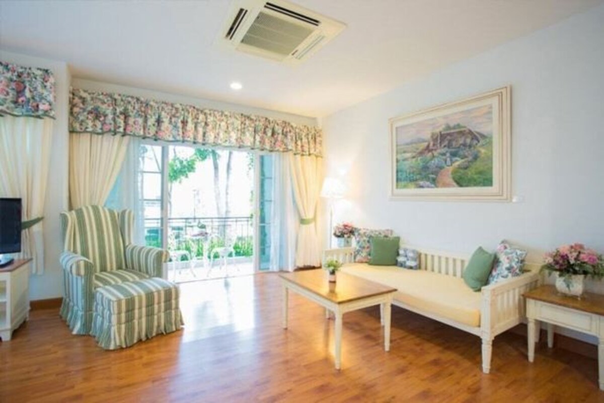 A living room with a sofa, armchair, and a coffee table. There is a painting on the wall and a window with curtains.
