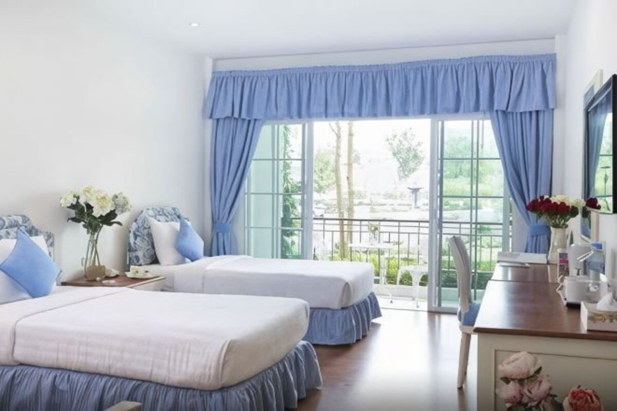 A hotel room with two beds, a desk, and a view of the outdoors.