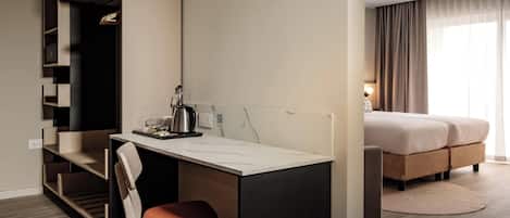 A modern hotel room with a desk, chair, and a bed with a large window.