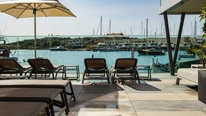 A terrace with lounge chairs and tables overlooking a marina with boats. - Strand Suites By Neu Collective (Gzira)