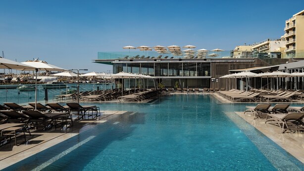 A swimming pool with sun loungers and umbrellas, surrounded by buildings with balconies. - Strand Suites By Neu Collective (Gzira)