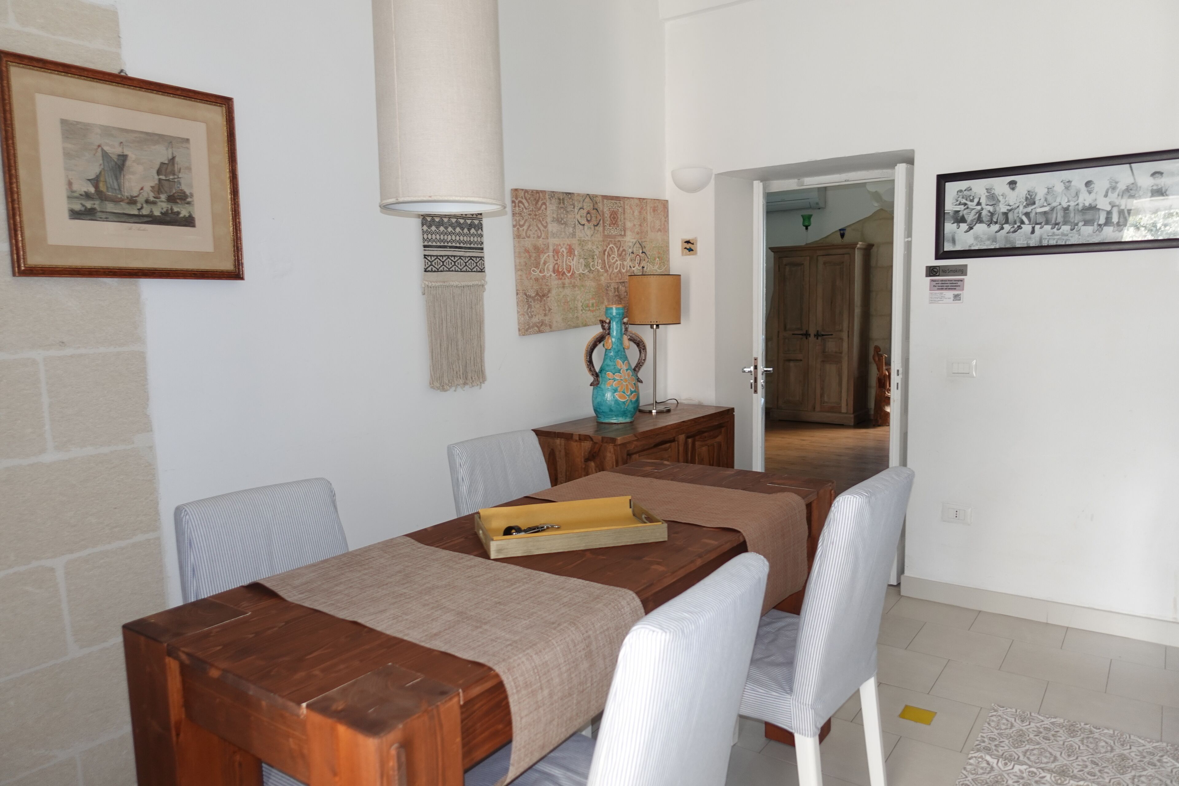 A dining area with a wooden table, white chairs, a lamp, and a framed picture on the wall.