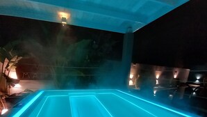 A heated outdoor pool with blue LED lighting, surrounded by lounge chairs and a small table. - Masseria Villa Marchesi (Taranto)