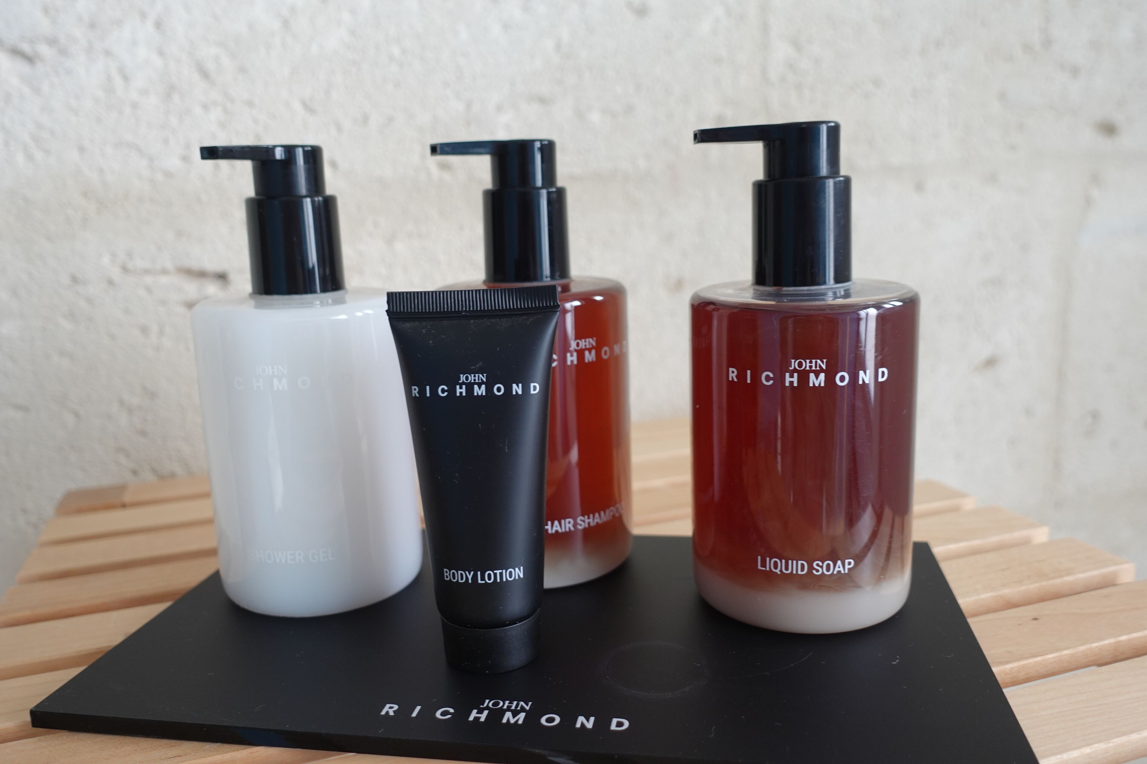 Quatro produtos de cuidados para o corpo John Richmond sobre um tabuleiro preto.