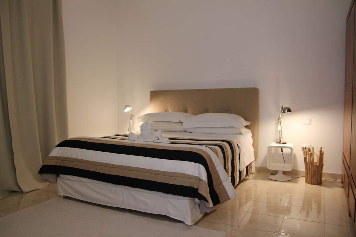 Uma cama bem arrumada com um edredom listrado, duas luminárias de cabeceira e uma mesa de cabeceira com abajur.