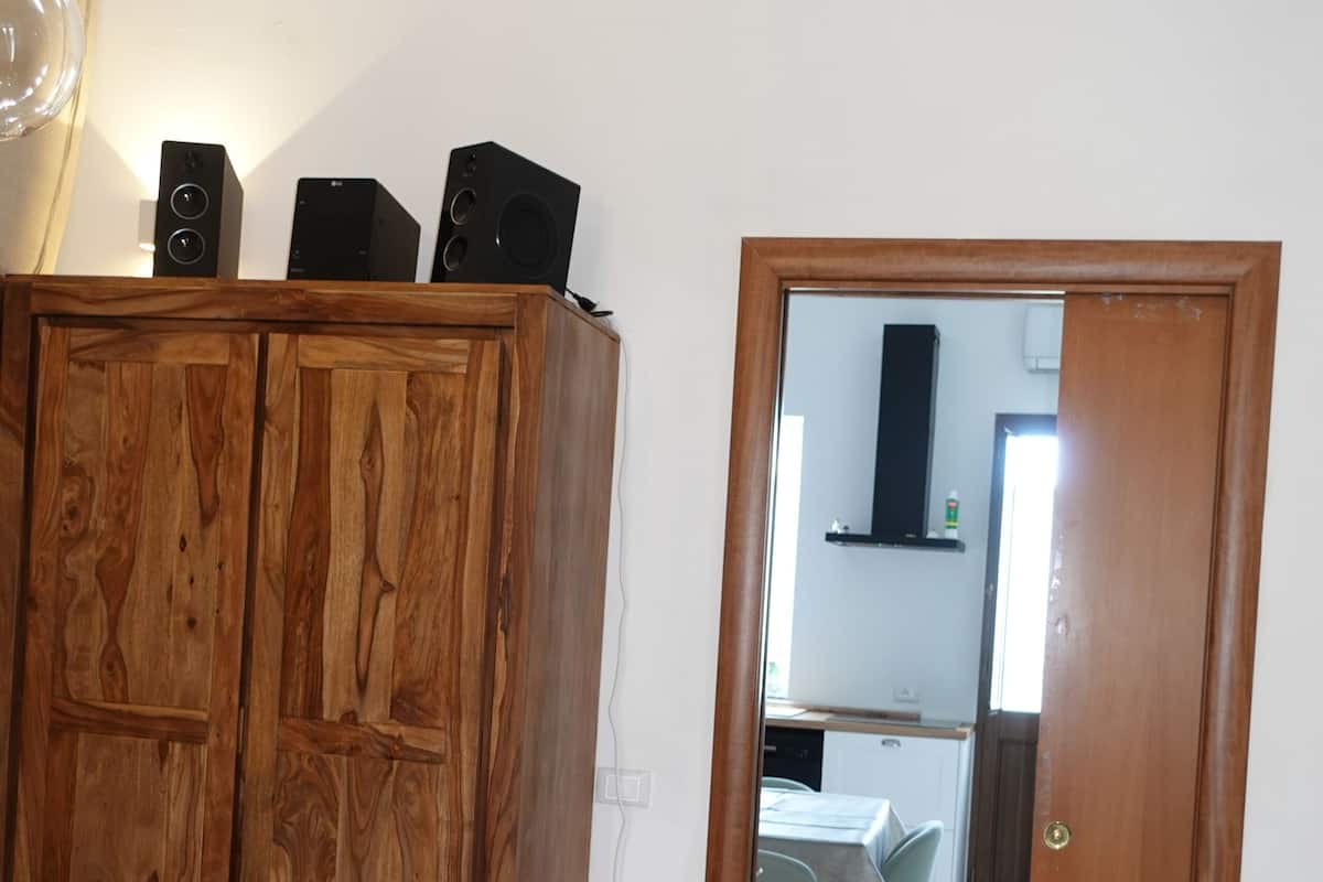 Um guarda-roupa de madeira com colunas de som, um banquinho pequeno e uma porta que dá para uma cozinha.