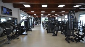 A gym with various exercise machines, large windows, and a wooden ceiling. - Masseria Villa Marchesi (Taranto)