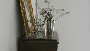 Een houten dressoir met een spiegel, een lamp en een vaas met bloemen.