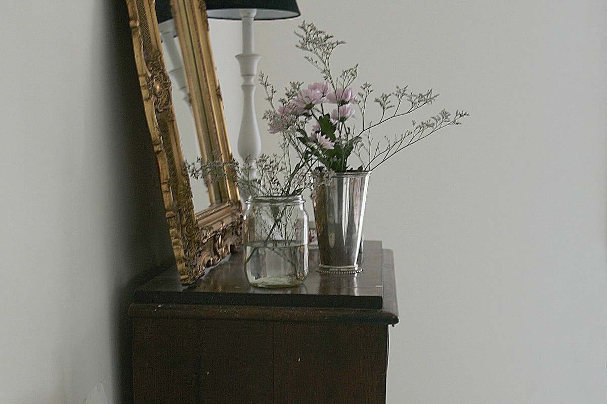 A wooden dresser with a mirror, a lamp, and a vase with flowers.