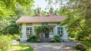 Een huis met een grindpad, een veranda met witte stoelen en een tuin met diverse planten.