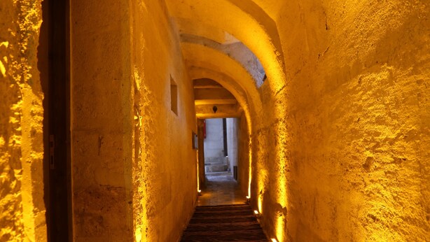 A narrow, arched corridor with stone walls and a wooden floor, illuminated by warm lighting. - Avanos Suites (Avanos)