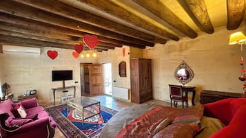 Una habitación amplia con una cama grande, techo de madera, sofá rojo, alfombra estampada y televisión en la pared.