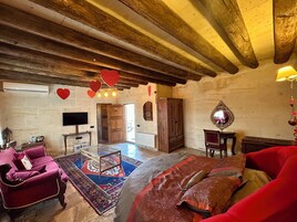 A spacious room with a large bed, a wooden ceiling, a red sofa, a patterned rug, and a television on the wall.