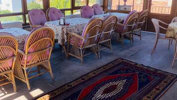 Un patio iluminado por el sol con muebles de mimbre, una alfombra estampada y vistas de edificios al fondo.