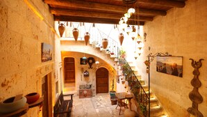 A narrow, sunlit corridor with a wooden ceiling, a staircase, and hanging pottery. - Avanos Suites (Avanos)