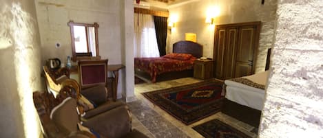 A rustic room with a wooden ceiling, a bed with a red bedspread, a wooden wardrobe, and a small table with a lamp.