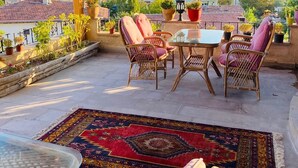 A covered outdoor seating area with wicker furniture and a glass table, overlooking a cityscape with buildings and mountains. - Avanos Suites (Avanos)