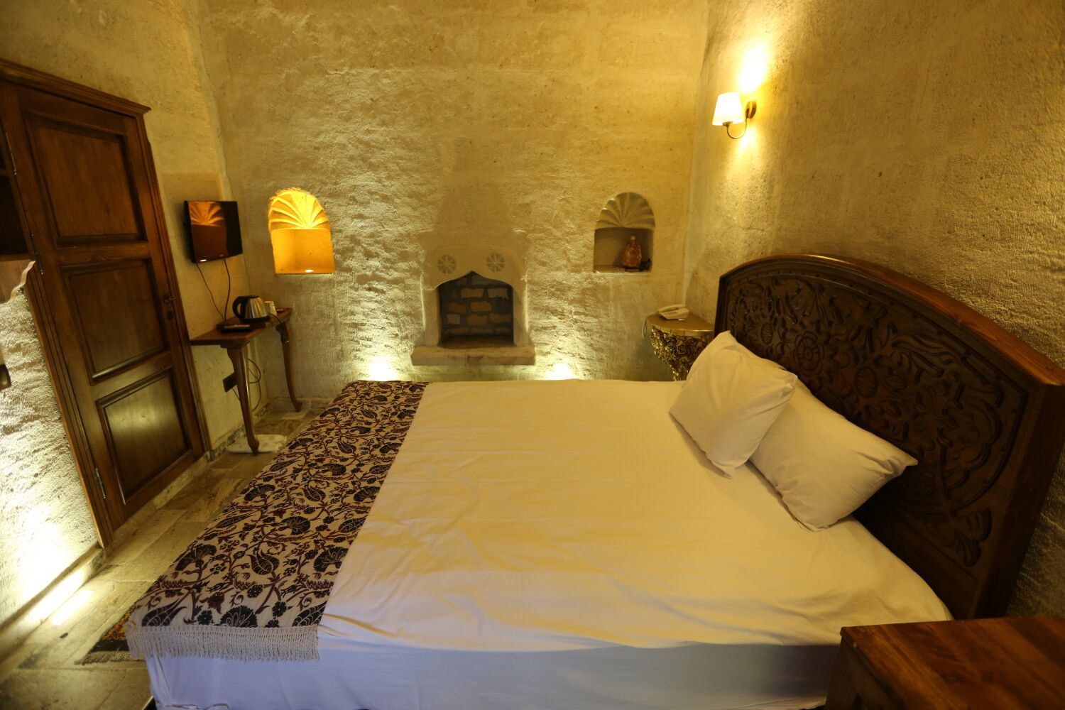 Une chambre à coucher comprenant un lit, une table de chevet, une armoire en bois et un mur en pierre avec une cheminée.