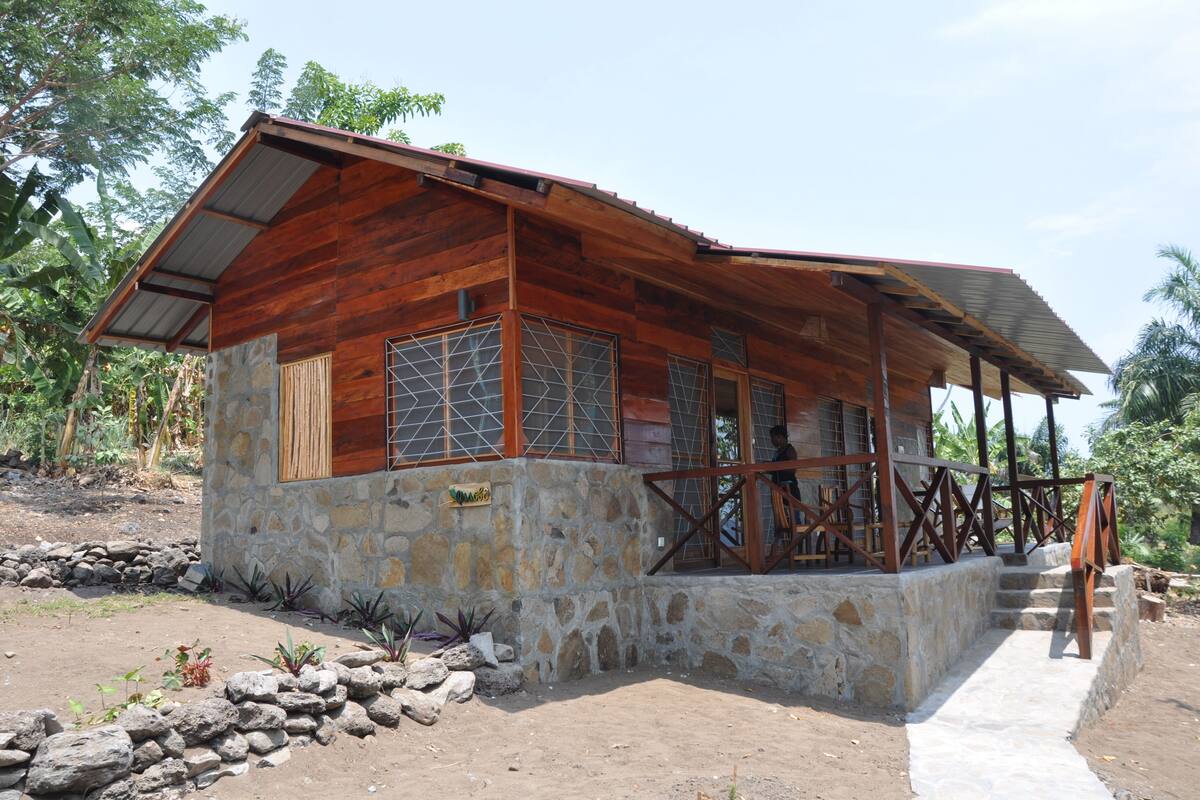 A rustic wooden house with a stone foundation, large windows, and a porch area.