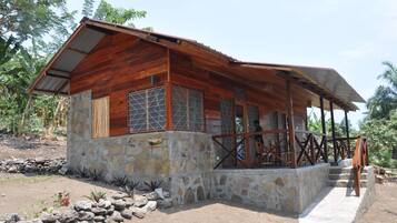 A rustic wooden house with a stone foundation, large windows, and a porch area.