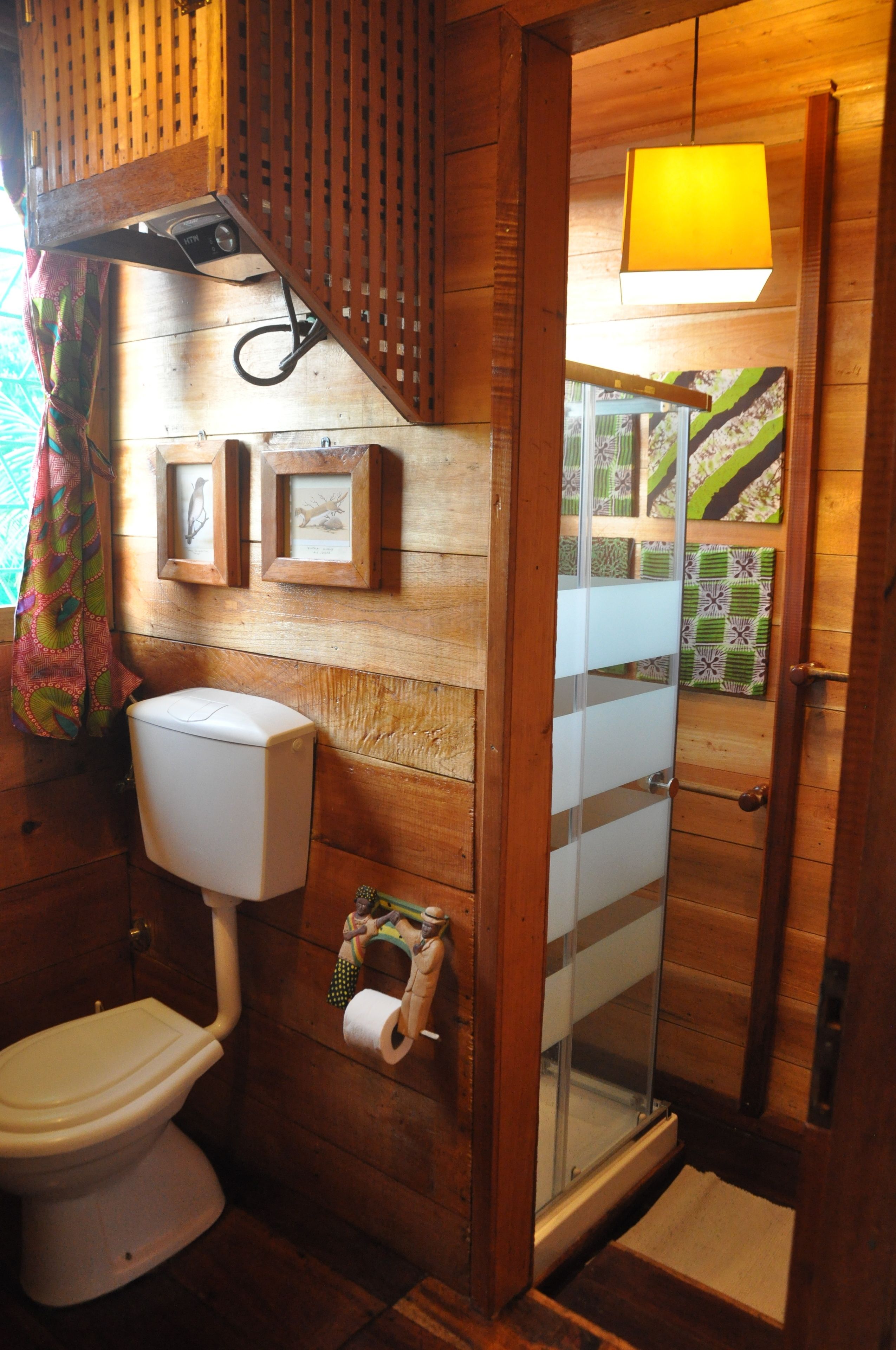 A wooden bathroom with a toilet, a glass shower enclosure, and framed pictures on the wall.