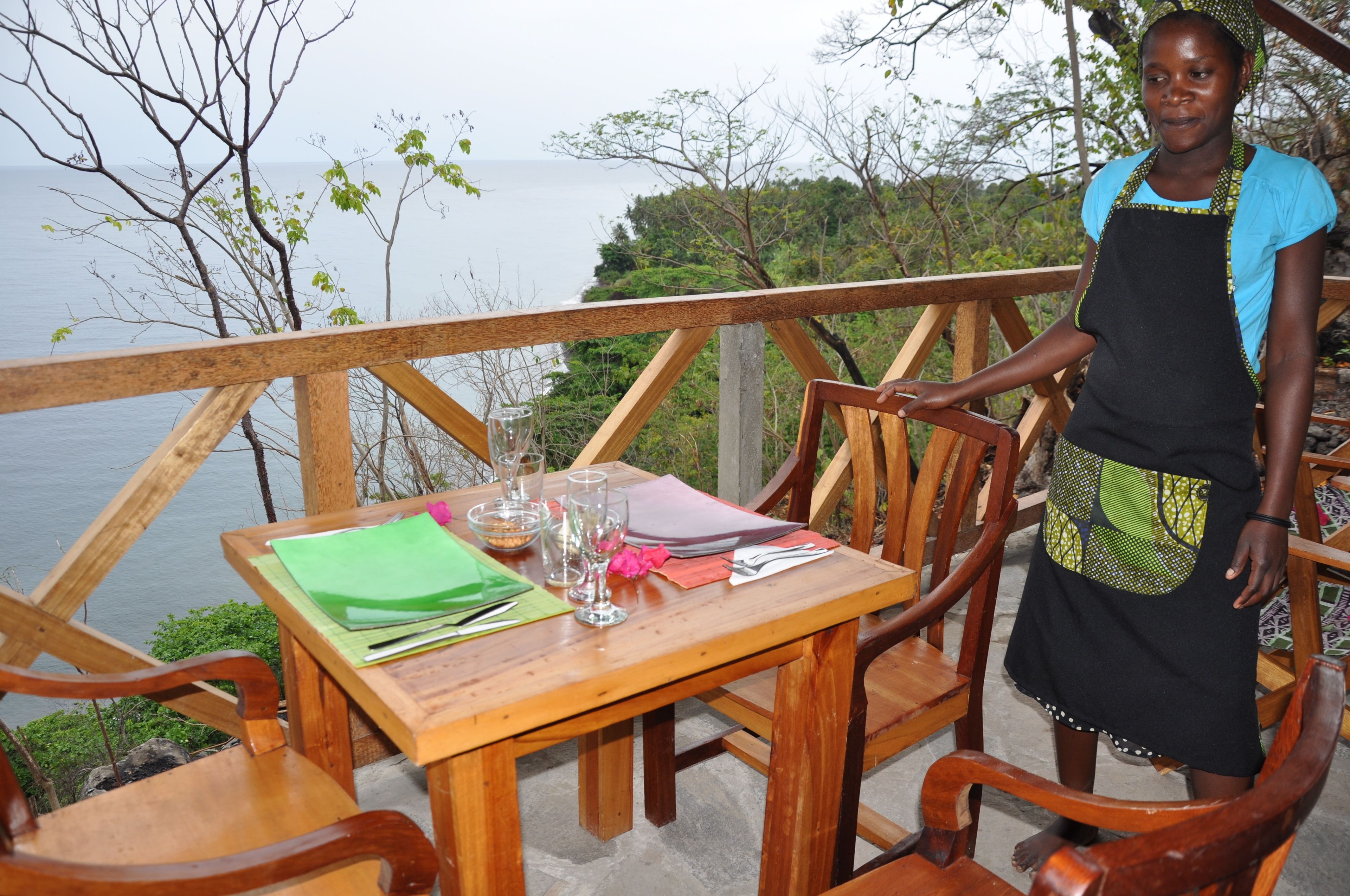 A wooden table with a view of the sea, surrounded by wooden chairs.