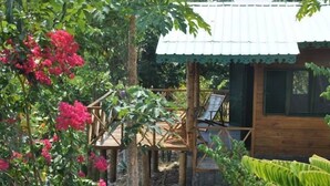 A wooden cabin with a metal roof, surrounded by lush greenery and flowering plants. - Mucumbli Hotel (Neves)