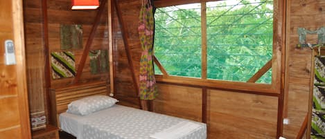A wooden cabin room with a bed, a window, and a ceiling fan.