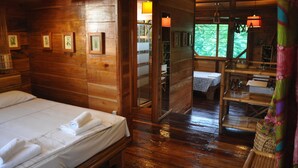 A wooden cabin room with a bed, a wooden bench, and a small table with a lamp. - Mucumbli Hotel (Neves)