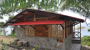 A rustic cabin with a stone exterior, wooden window shutters, and a red metal roof. - Mucumbli Hotel (Neves)