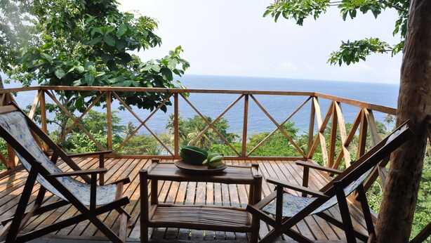 A wooden deck with a table and two chairs, overlooking a scenic view of the ocean and lush greenery. - Mucumbli Hotel (Neves)