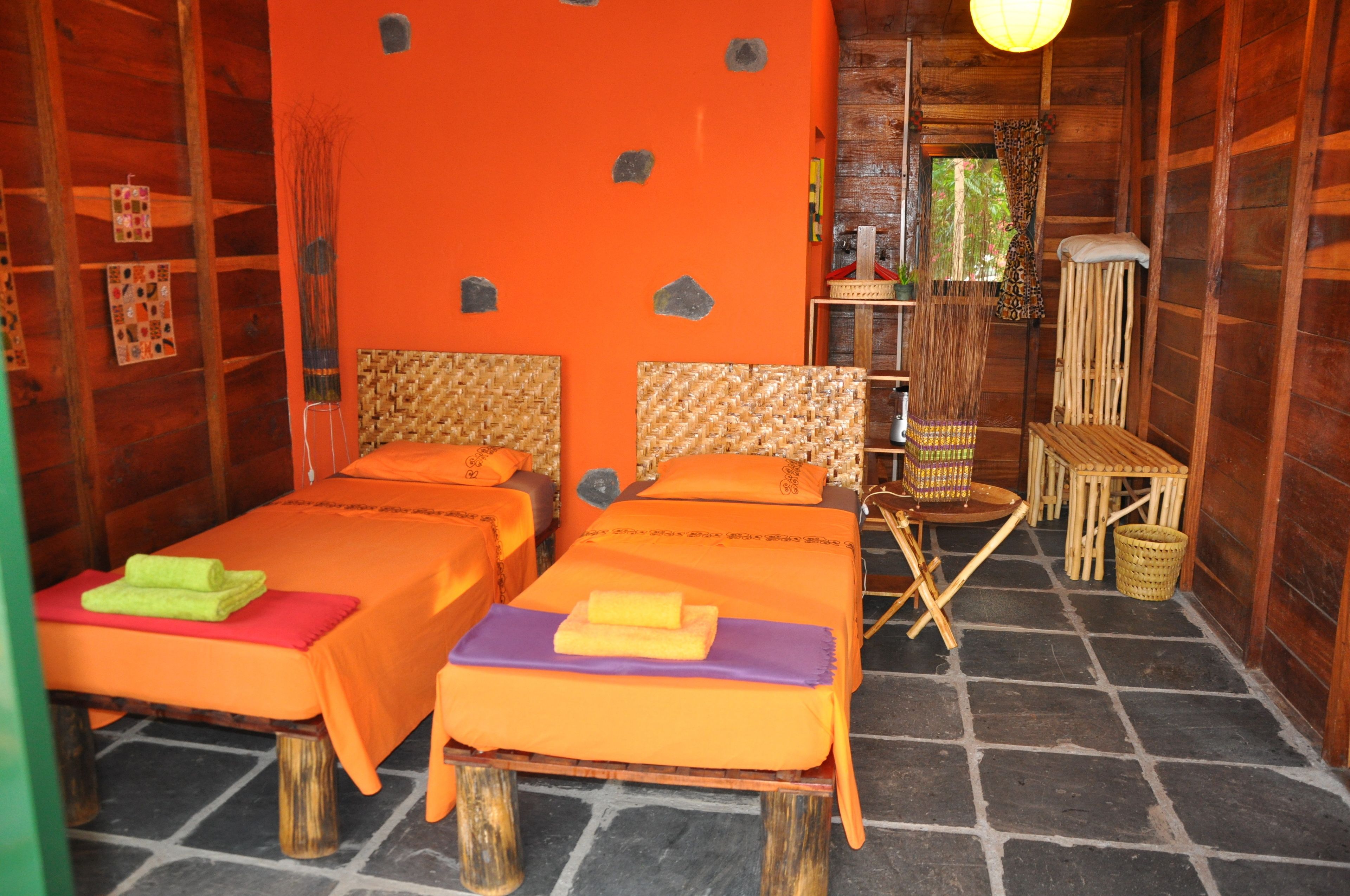 A room with two beds, a wooden floor, and a bright orange wall.