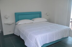 A bed with a teal headboard, white bedding, and a white wall with a light switch and a small shelf. - B&B Il Paradiso di Capri (Anacapri)