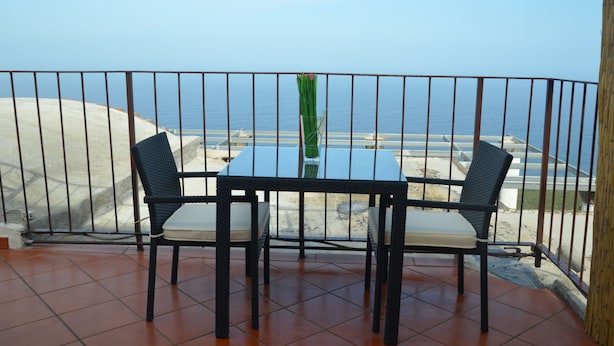 A balcony with a table and chairs, overlooking a beach and the sea.