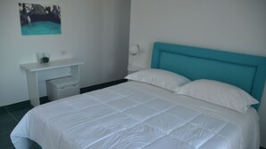 A bedroom with a large bed, a white nightstand, and a wall-mounted shelf.