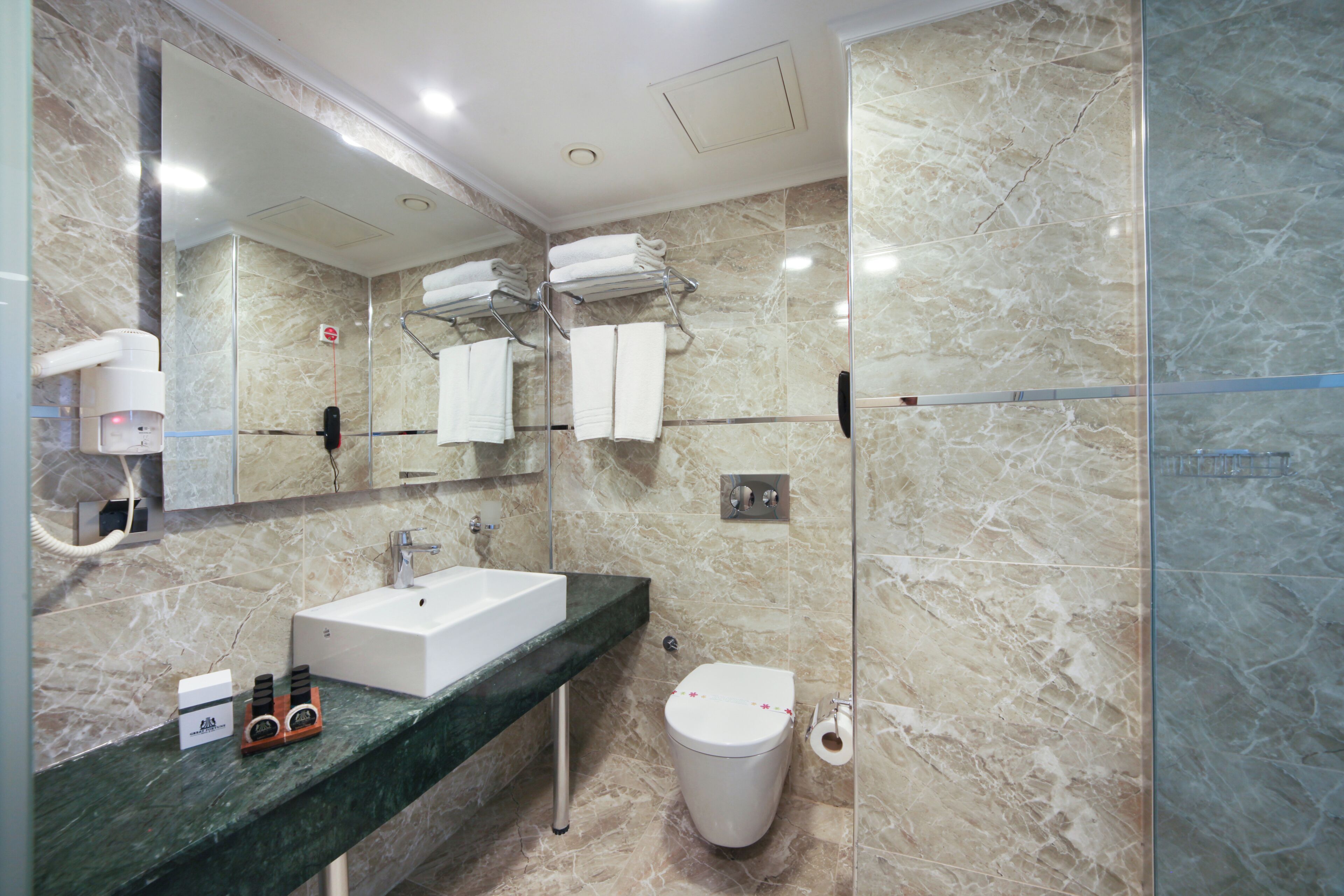 A modern bathroom with a marble sink, a large mirror, a towel rack, and a toilet.