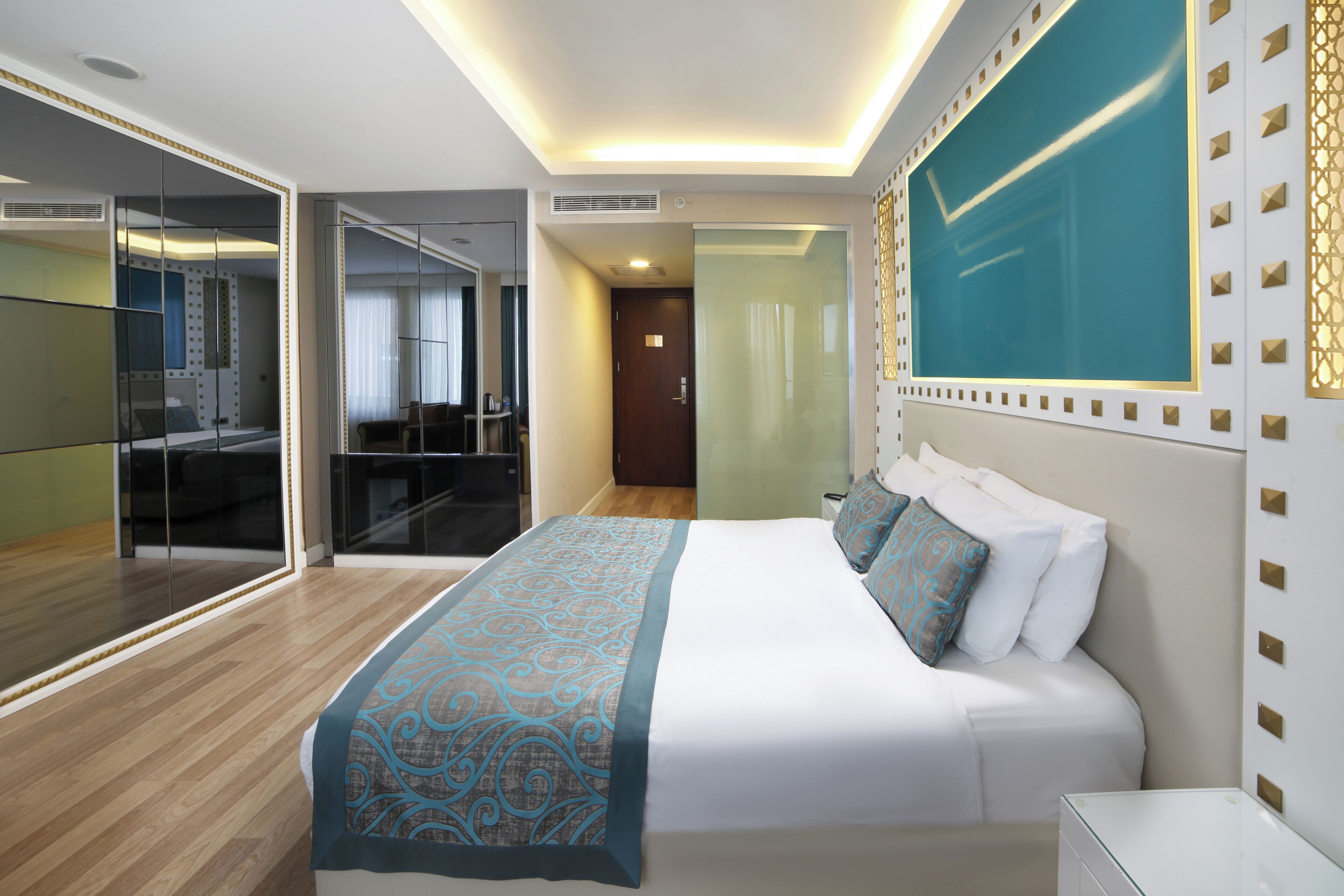 A hotel room with a large bed, a glass partition, a desk, and a view of the city.