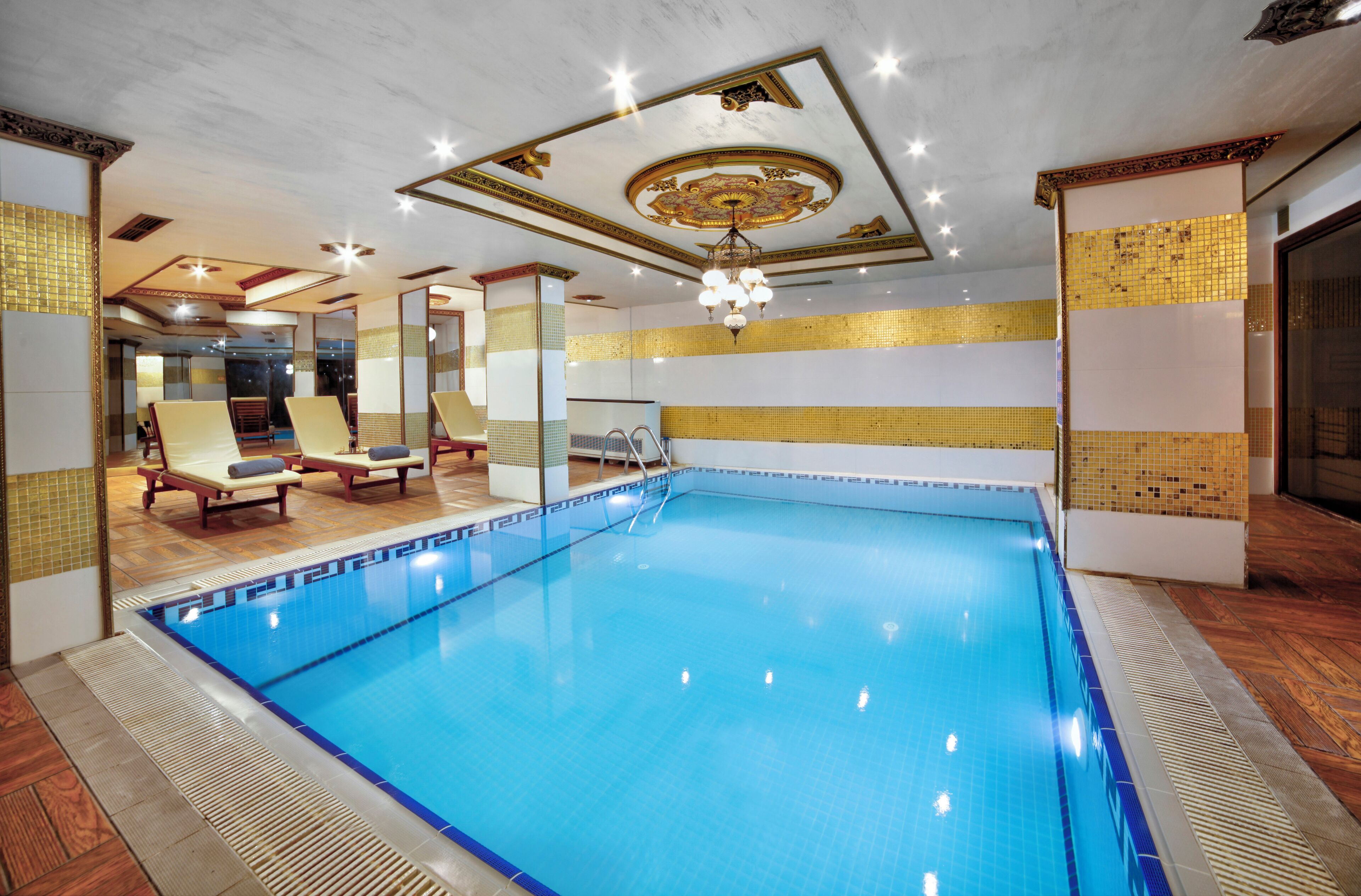 A swimming pool with lounge chairs, a ceiling with decorative elements, and a tiled wall.