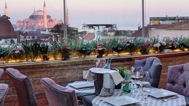Un restaurant où une table est dressée pour le dîner, avec vue sur un bâtiment historique et agrémenté d’une composition florale décorative.