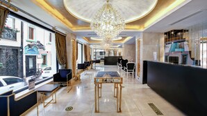 Un hall d’hôtel avec un lustre, un espace salon, un comptoir d’accueil et une vue sur la rue.