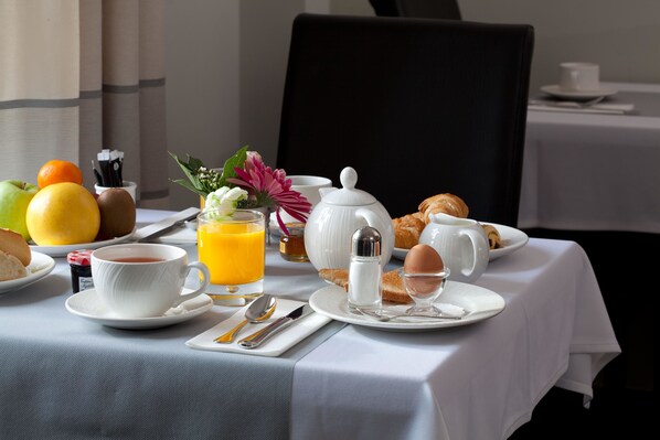 Una mesa de desayuno servida con una taza de té, jugo de naranja, croissants y un bol de fruta.