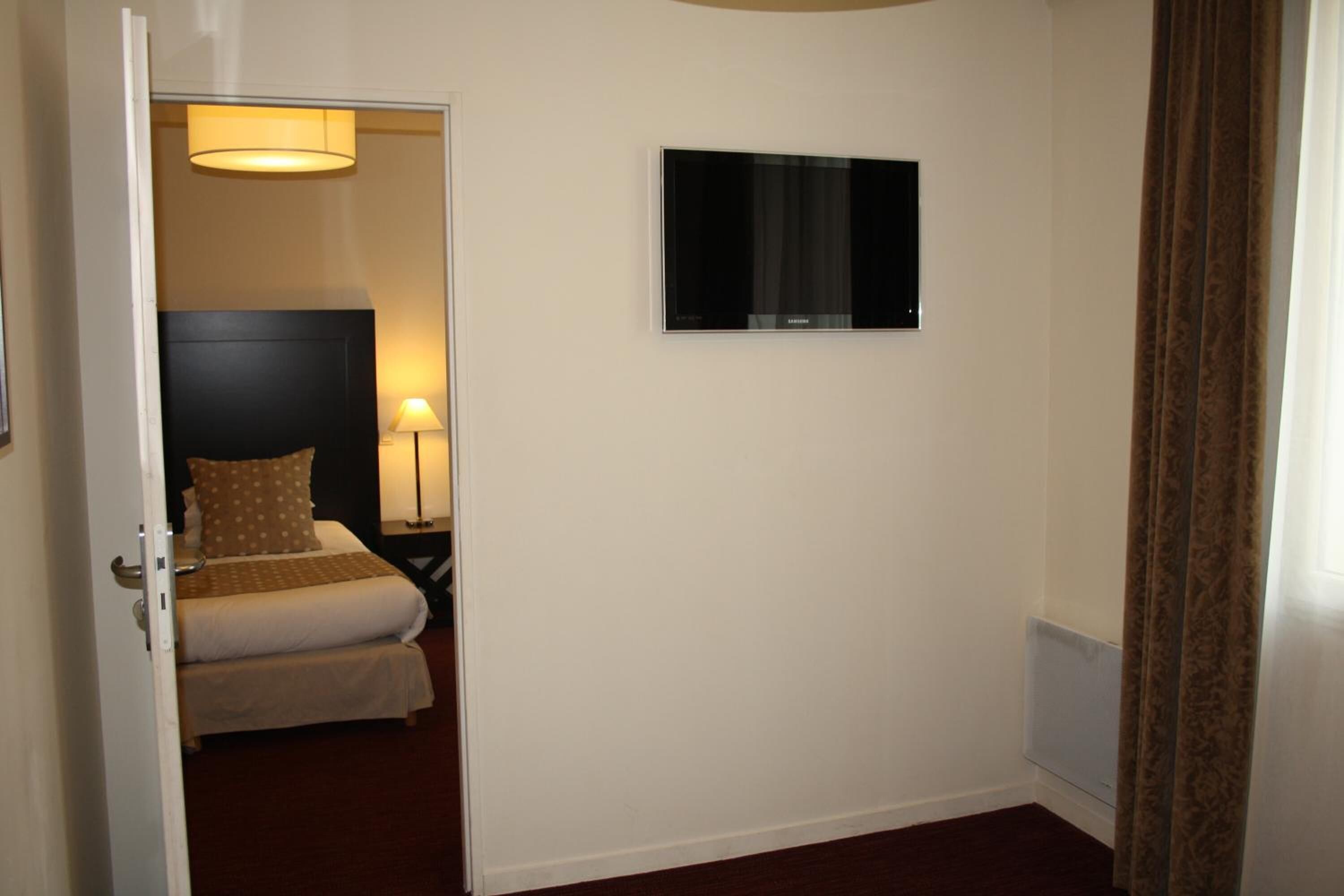 Una camera d'albergo con un letto, una televisione montata a parete e una porta che dà su un'altra stanza.