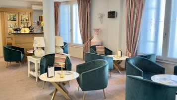 A modern lounge area with teal armchairs, a round table, and a bar area with liquor bottles.