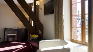 Una habitación con una escalera de madera, un escritorio con una silla, un televisor y una ventana con cortinas.