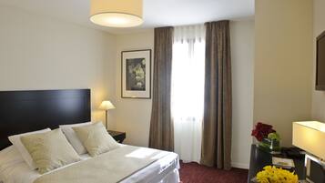 A hotel room with a large bed, a nightstand, a lamp, a framed picture on the wall, and a window with curtains.