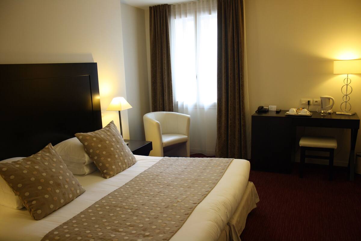 A hotel room with a large bed, a desk, a chair, and a TV.