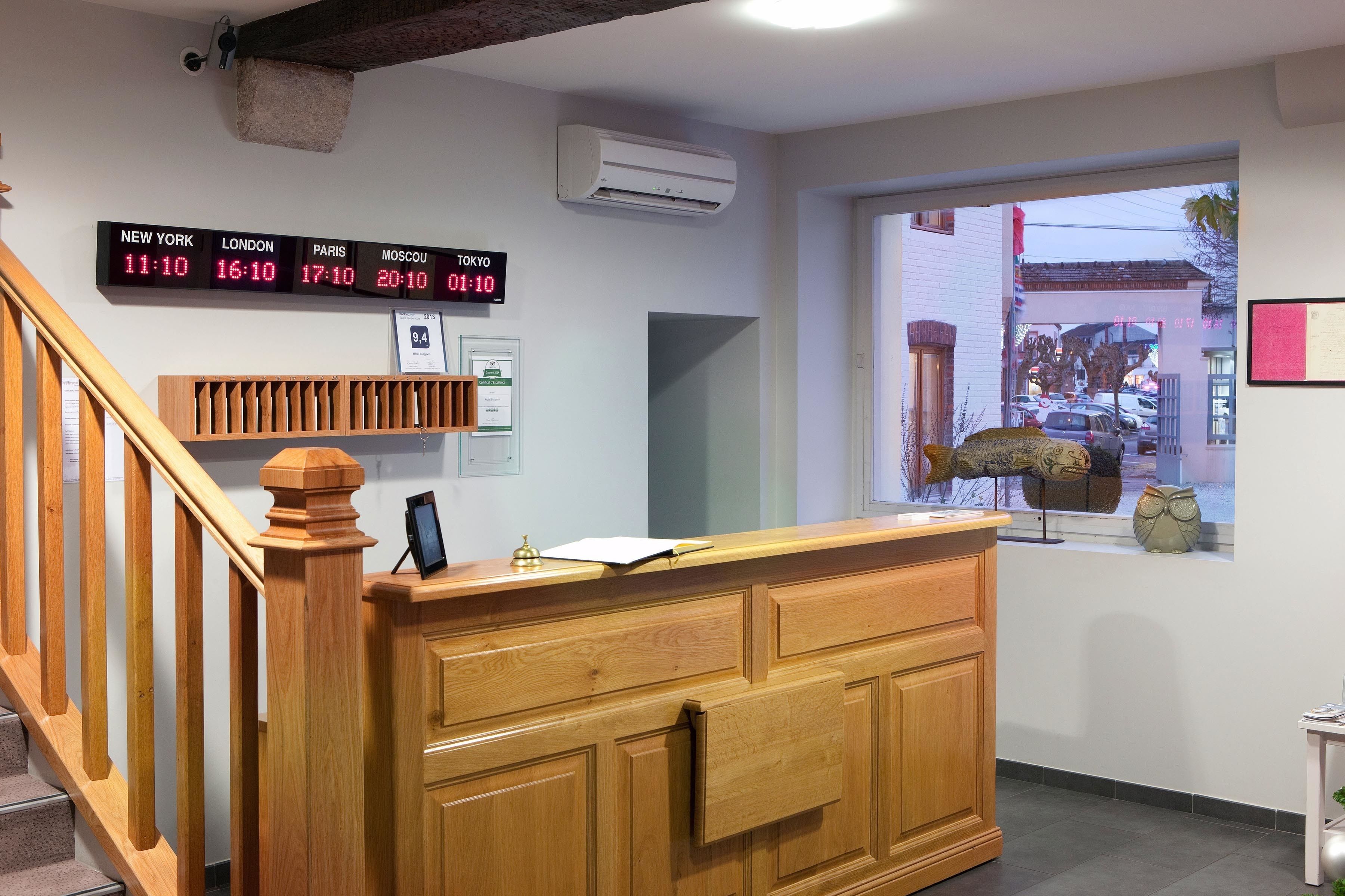 Una recepción con un reloj digital que muestra la hora en varias ciudades, una escalera de madera y un ventanal con vistas al exterior.