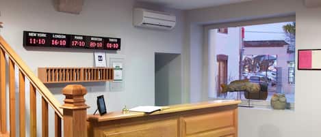 Una recepción con un reloj digital que muestra la hora en varias ciudades, una escalera de madera y un ventanal con vistas al exterior.